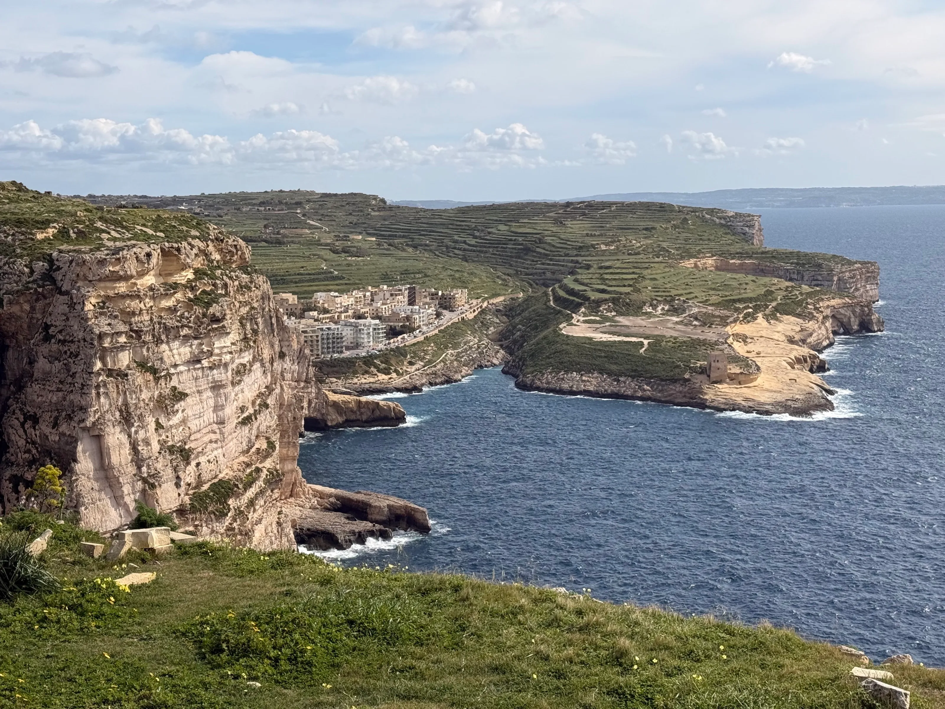 Steilküste über einer Bucht, dahinter terrassierte Felder und ein weißer Ort am Wasser